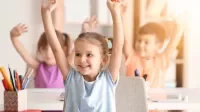 Lächelnde Kinder heben die Hände im Unterricht