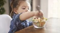 Kind isst Obst mit einer Gabel aus einer Glasschale