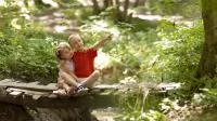 Zwei Kinder sitzen auf einer Brücke im Wald