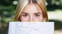 Frau hält ein Heft mit Matheaufgaben vor das Gesicht. Bild von Freepik
