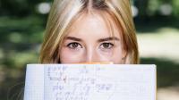 Frau hält ein Heft mit Matheaufgaben vor das Gesicht. Bild von Freepik