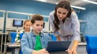 Ein Schüler arbeitet an einem Tablet und eine Lehrerin erklärt ihm etwas.