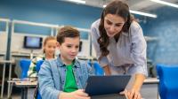 Ein Schüler arbeitet an einem Tablet und eine Lehrerin erklärt ihm etwas.