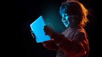 Ein Schulkind blickt auf einen leuchtenden Tablet-Computer, den es in den Händen hält