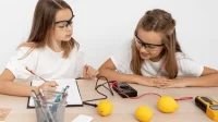 ZWei Mädchen bauen eine Zitronen-Uhr und machen Notizen zu ihrem Experiment
