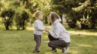 Eine Mutter spricht mit ihrem Kind in einem Park und hält dessen Hände