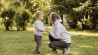 Eine Mutter spricht mit ihrem Kind in einem Park und hält dessen Hände