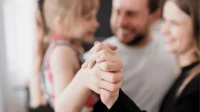 Ein Elternpaar hält ihre Tochter im Arm und dabei ihre Hand