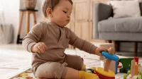 Ein Baby sitzt auf dem Boden und baut aus bunten Ringen einen Turm