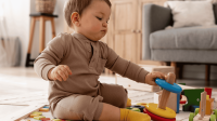 Ein Baby sitzt auf dem Boden und baut aus bunten Ringen einen Turm