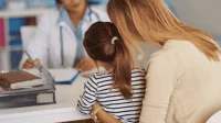 Eine Mutter sitzt mit ihrem Kind bei der Schuleingangsuntersuchung vor einer Ärztin