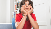 Ein Schulkind sitzt grübelnd an seinem Schreibtisch und legt den Kopf in die Hände