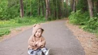 Kleinkind im Bärenkostüm sitzt auf einem Waldweg