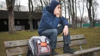 Jugendliche Person sitzt mit Schulranzen auf der Rücklehne einer Bank