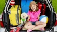 Mädchen mit Hund und Urlaubsgepäck im Kofferraum