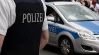Foto eines Polizisten in Schutzweste vor Polizeiautos