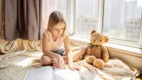 Foto eines Mädchens mit Teddy beim Lesen