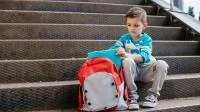 Foto eines kleinen Jungen mit seinem Ranzen auf einer Treppe
