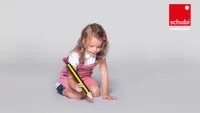 Kind sitzt auf dem Boden und schreibt mit einem riesigen Stift