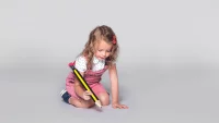 Kind sitzt auf dem Boden und schreibt mit einem riesigen Stift