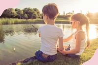 Zwei Kinder sitzen an einem See und angeln in der Sonne