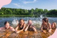 Kinder halten sich im Badesee an einem Steg fest und planschen mit den Beinen im Wasser