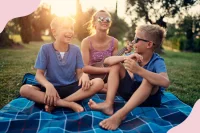Drei Kinder sitzen auf einer Picknickdecke im Park in der Sonne