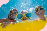 Eine Familie mit gelben Sonnenbrillen schwimmt zusammen auf einer gelben Luftmatratze im Wasser