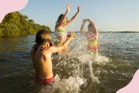 Kinder toben in Badekleidung in einem See und das Wasser spritzt nach oben