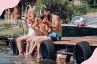 Eine Familie sitzt auf einem Steg am Wasser und isst Wassermelone