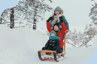 Eine Mutter fährt mit ihren beiden Kindern auf einem großen Schlitten durch den Schnee