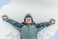 Ein Kind liegt mit ausgebreiteten Armen in Winterkleidung im Schnee