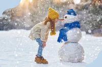 Ein Mädchen hält ihre Nase an die Möhren-Nase eines Schneemanns
