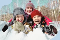 Drei Kinder liegen in Winterkleidung im Schnee und lachen