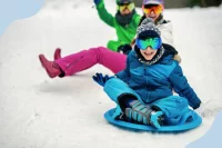 Kinder fahren auf bunten Rutsch-Schlitten einen verschneiten Hang hinab
