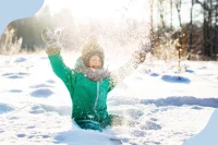 Ein Kind sitzt im verschneiten Wald und wirft glücklich Schnee in die Luft