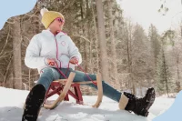 Ein Kind sitzt im verschneiten Wald auf einem Schlitten und lacht