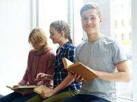 Drei Kinder sitzen auf einer Fensterbank und haben Bücher in der Hand