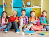 Kinder sitzen mit Schulmaterial vor einem Regal im Klassenzimmer