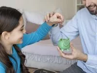 Mädchen und Vater packen Geld in eine Spardose