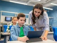 Ein Schüler arbeitet an einem Tablet und eine Lehrerin erklärt ihm etwas.