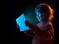 Ein Schulkind blickt auf einen leuchtenden Tablet-Computer, den es in den Händen hält