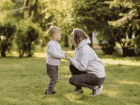 Eine Mutter spricht mit ihrem Kind in einem Park und hält dessen Hände