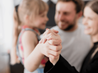 Ein Elternpaar hält ihre Tochter im Arm und dabei ihre Hand