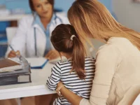 Eine Mutter sitzt mit ihrem Kind bei der Schuleingangsuntersuchung vor einer Ärztin