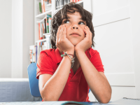 Ein Schulkind sitzt grübelnd an seinem Schreibtisch und legt den Kopf in die Hände
