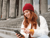 Junge Frau sitzt mit ihrem Smartphone vor einem Säulentempel