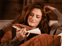 Eine Mutter liest entspannt ein Buch auf dem Sofa