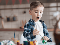 Ein Junge bemalt mit einem Pinsel und Farbe bunte Ostereier