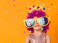 Ein Kind mit bunter Perücke und lustiger, großer Sonnenbrille wirft Konfetti in die Luft